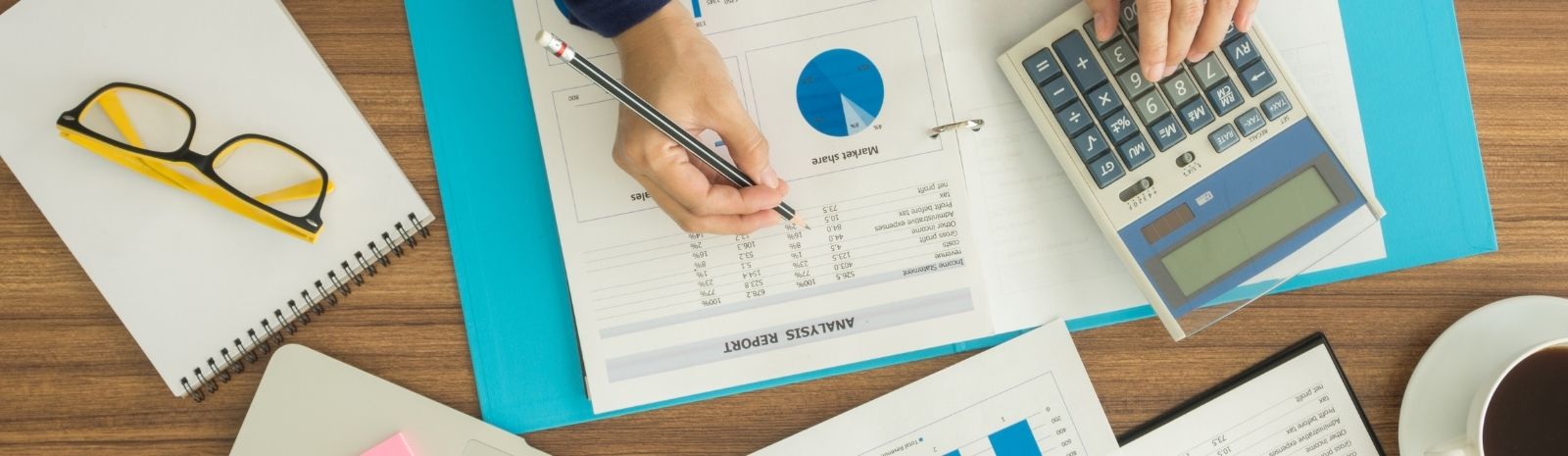 Running numbers on a spreadsheet with a calculator and yellow glasses on a desk